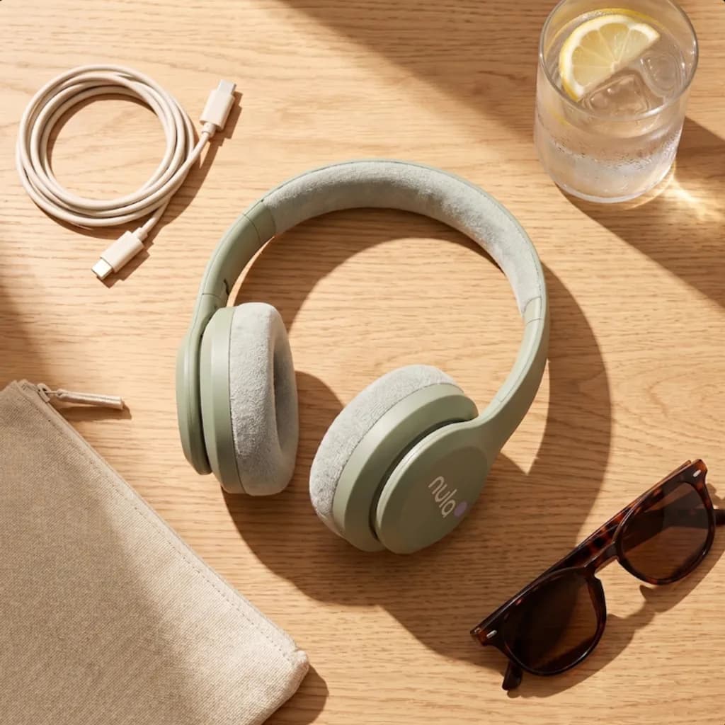 Nula Sage Mist headphones flat lay on oak with a charging cable and sunglasses