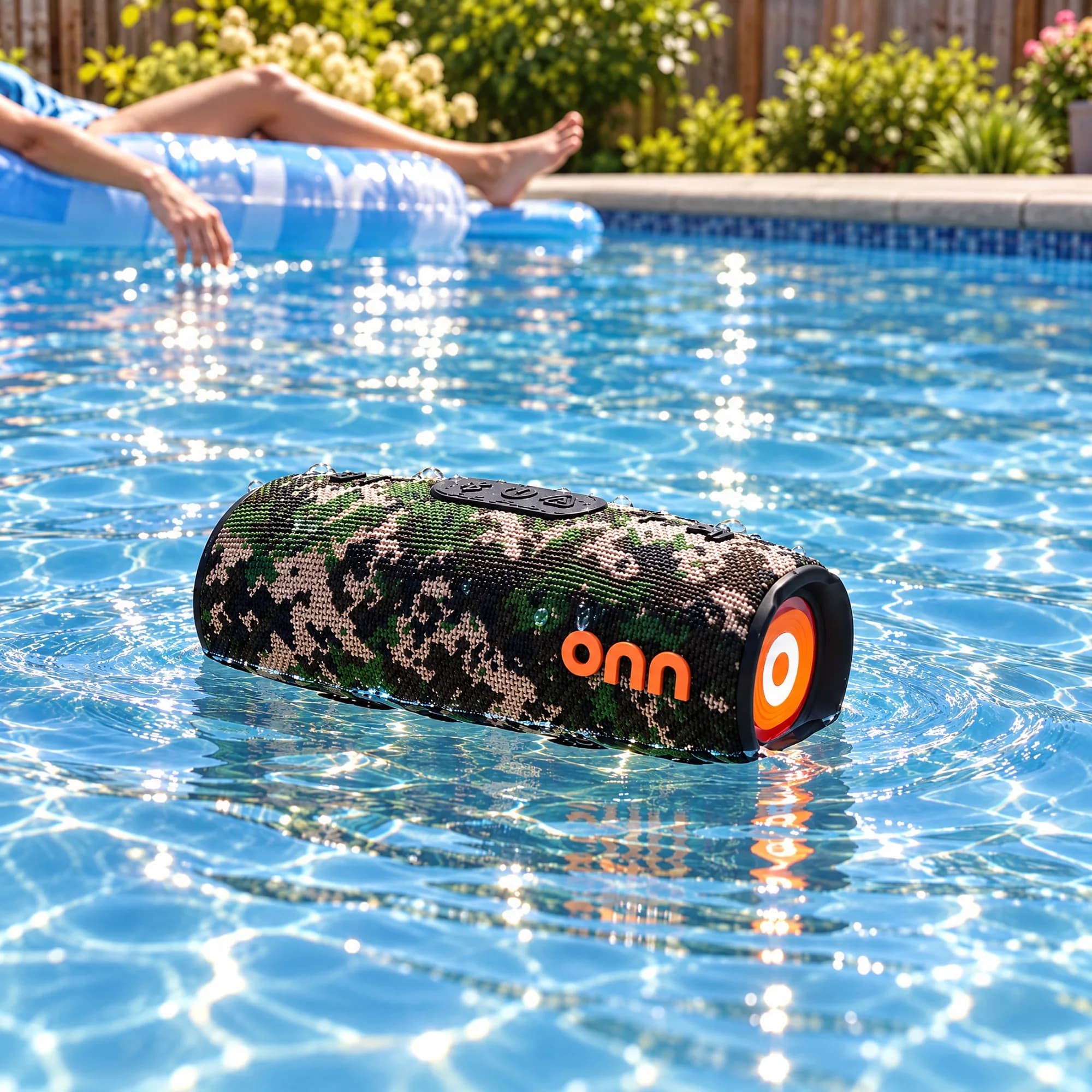 onn. camo rugged speaker floating in a swimming pool with a person relaxing on a blue raft in the background