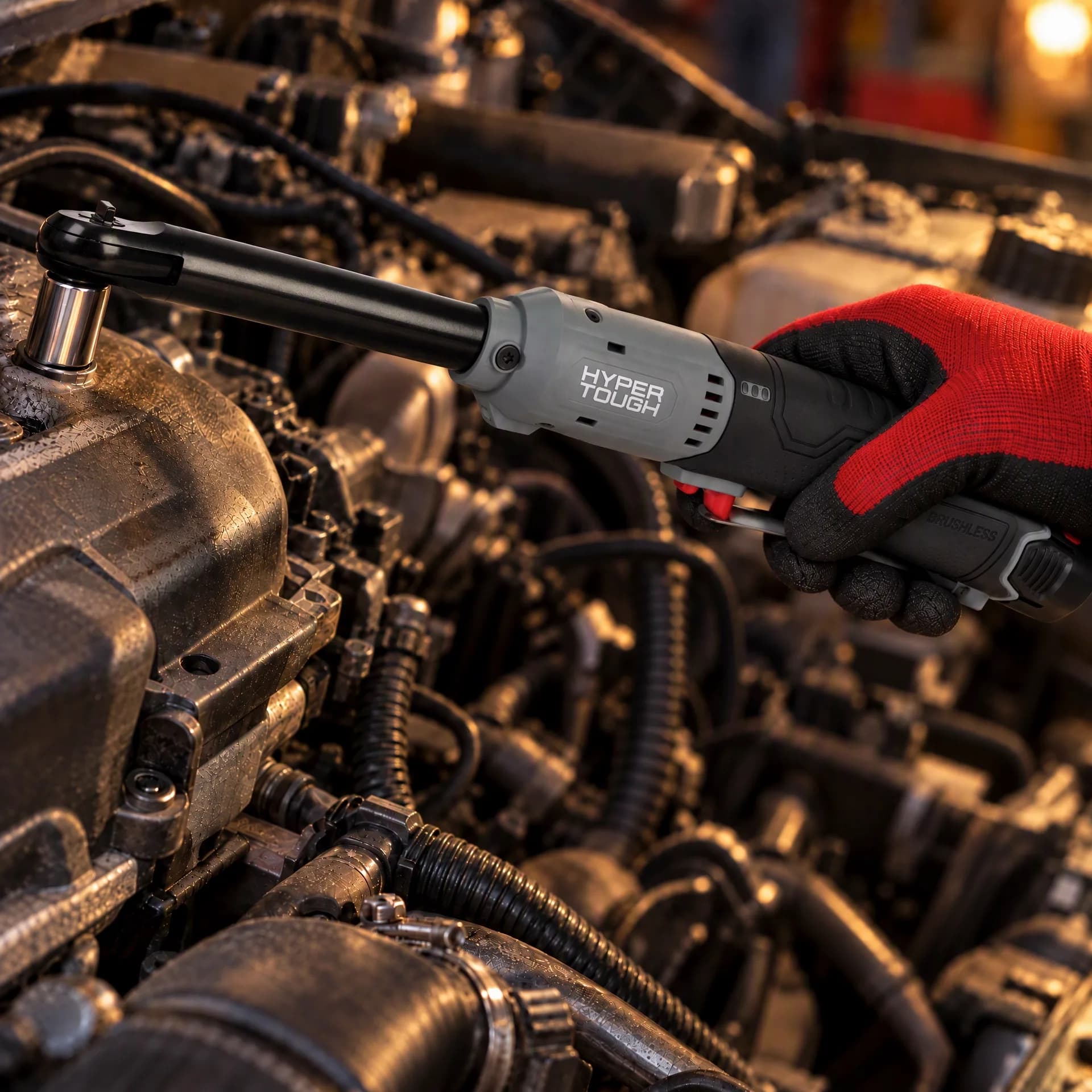 Gloved hand guiding the Hyper Tough extended reach ratchet wrench deep into a crowded engine bay to reach a fastener between hoses and wiring
