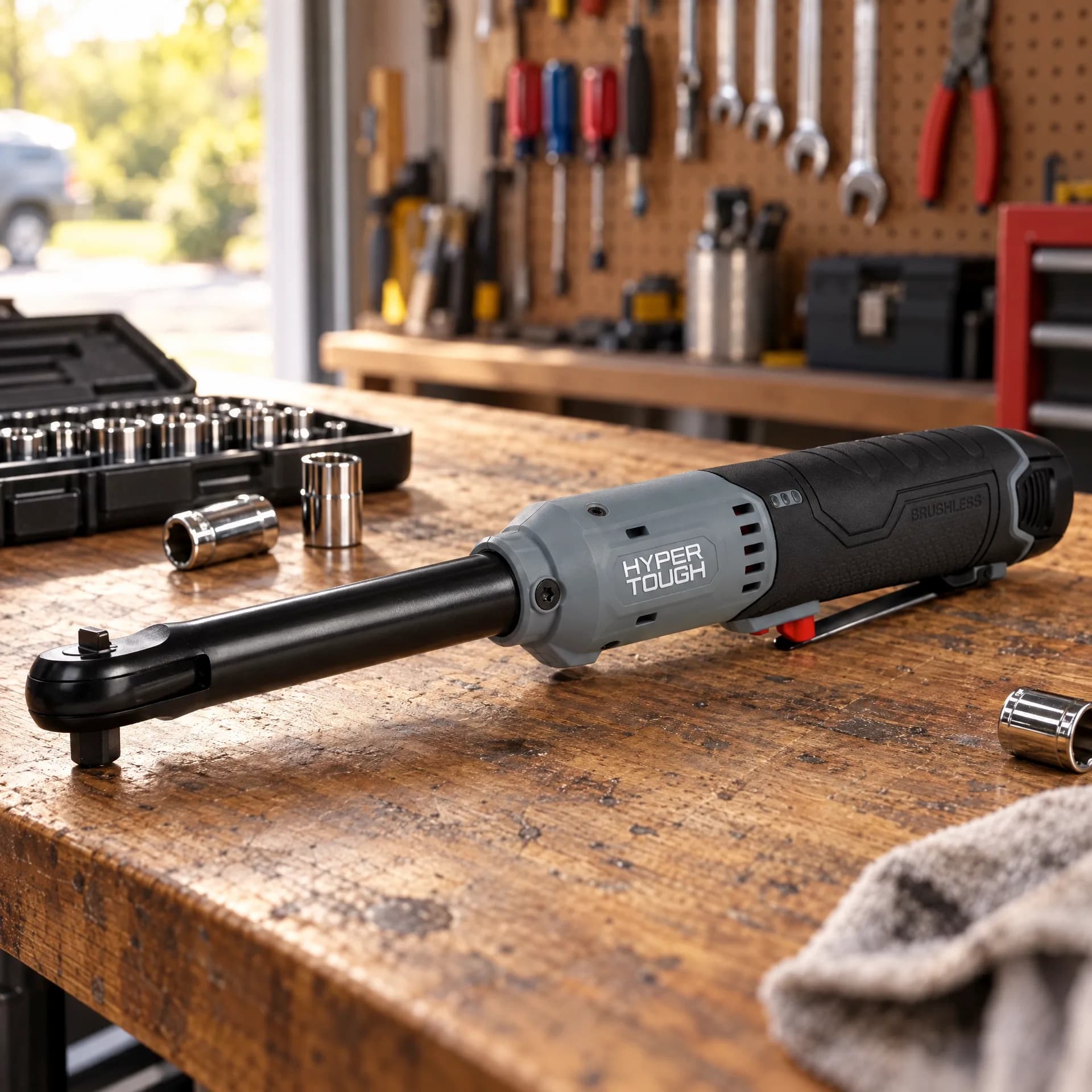 Hyper Tough extended reach ratchet wrench laid across a wooden workbench next to a socket case and loose chrome sockets, with a pegboard and red tool chest in the background